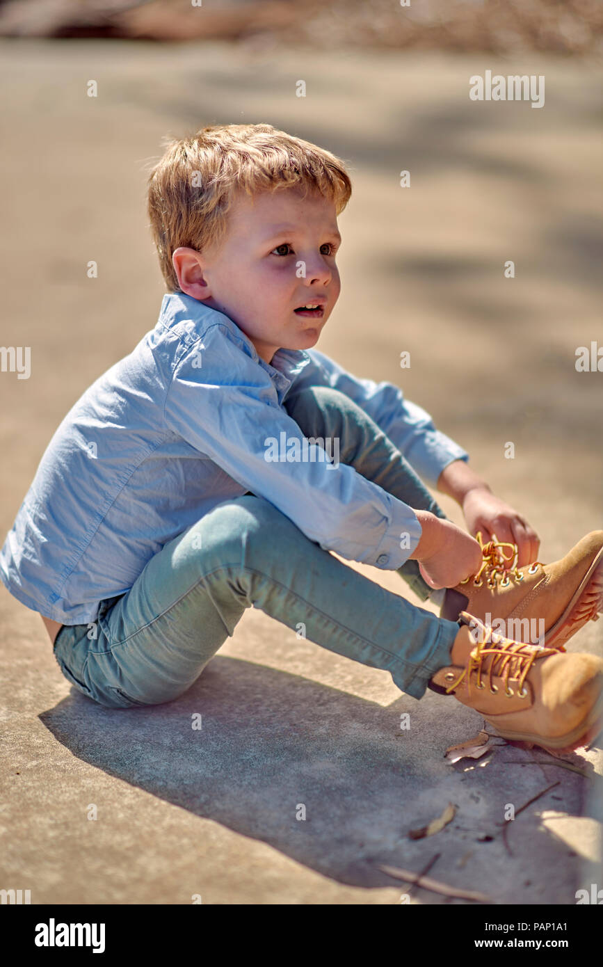 Boy sitting outdoors lacing his boots Stock Photo