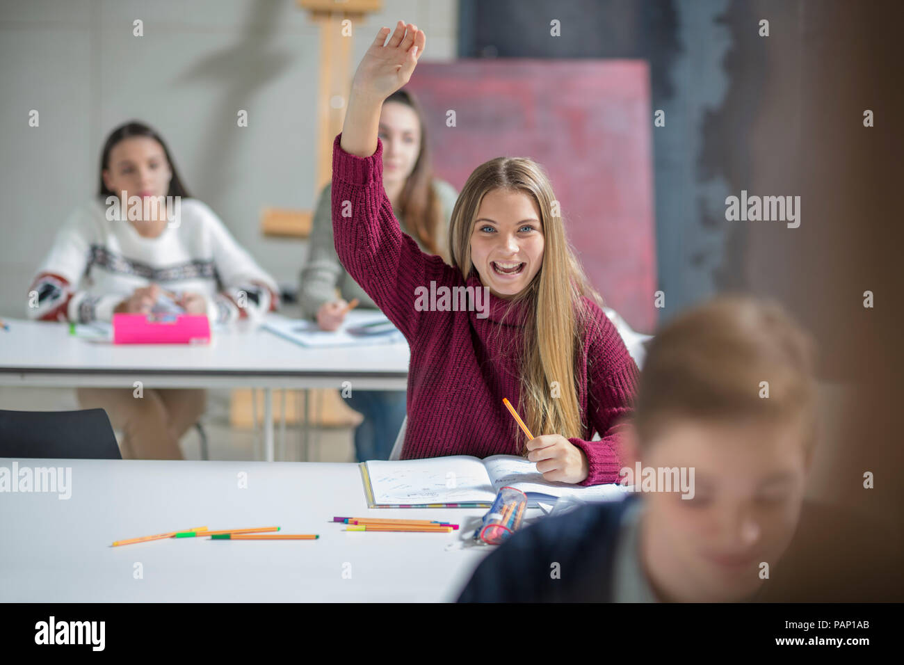 Happy teenage girl raising hand in class Stock Photo