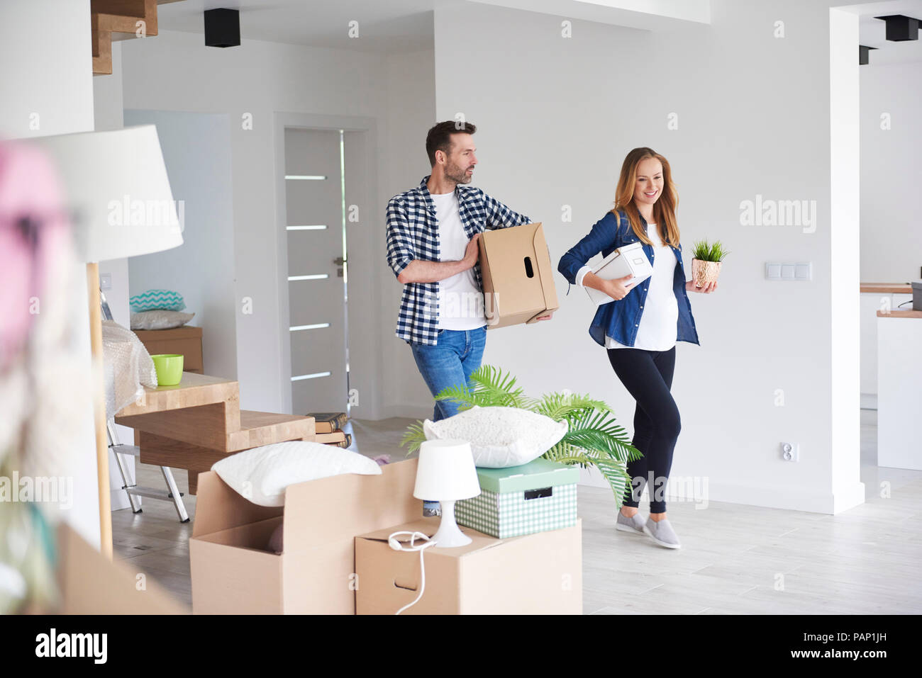 Couple Moving Into New Flat Carrying Cardboard Box And Plant Stock