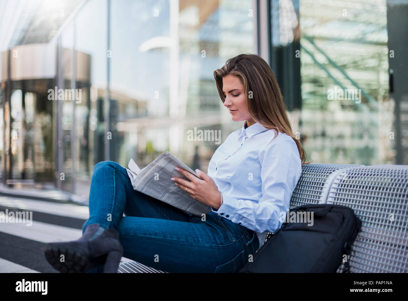 Portrait of young businesswoman sitting on bench reading newspaper Stock Photo