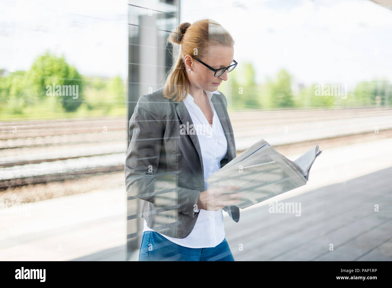 Mature businesswoman waiting at platform reading newspaper Stock Photo
