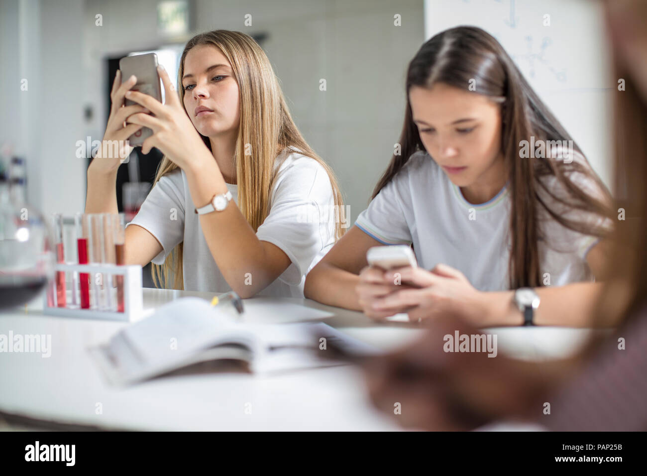 Teenage girls using cell phones in science class Stock Photo