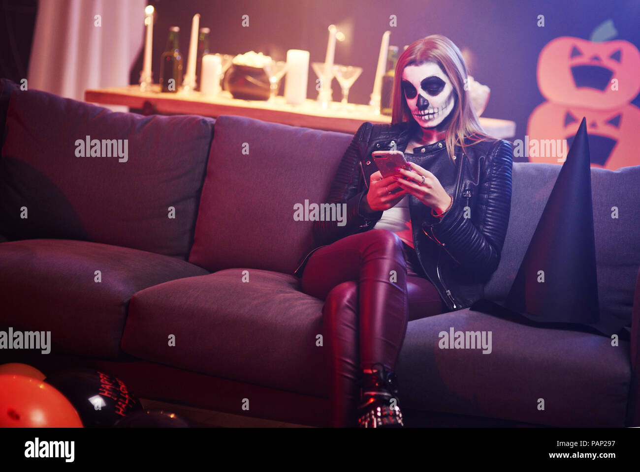 Bored woman using mobile phone at Halloween party Stock Photo