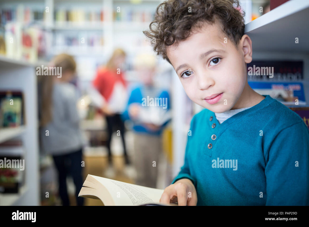 Portrait of smiling schoolboy with book in school library Stock Photo