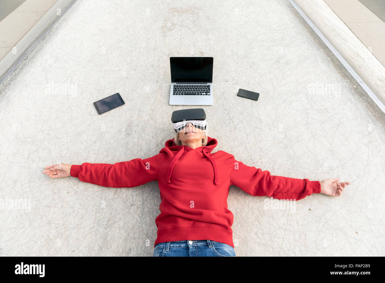 Senior woman lying on the ground wearing VR glasses next to mobile devices Stock Photo