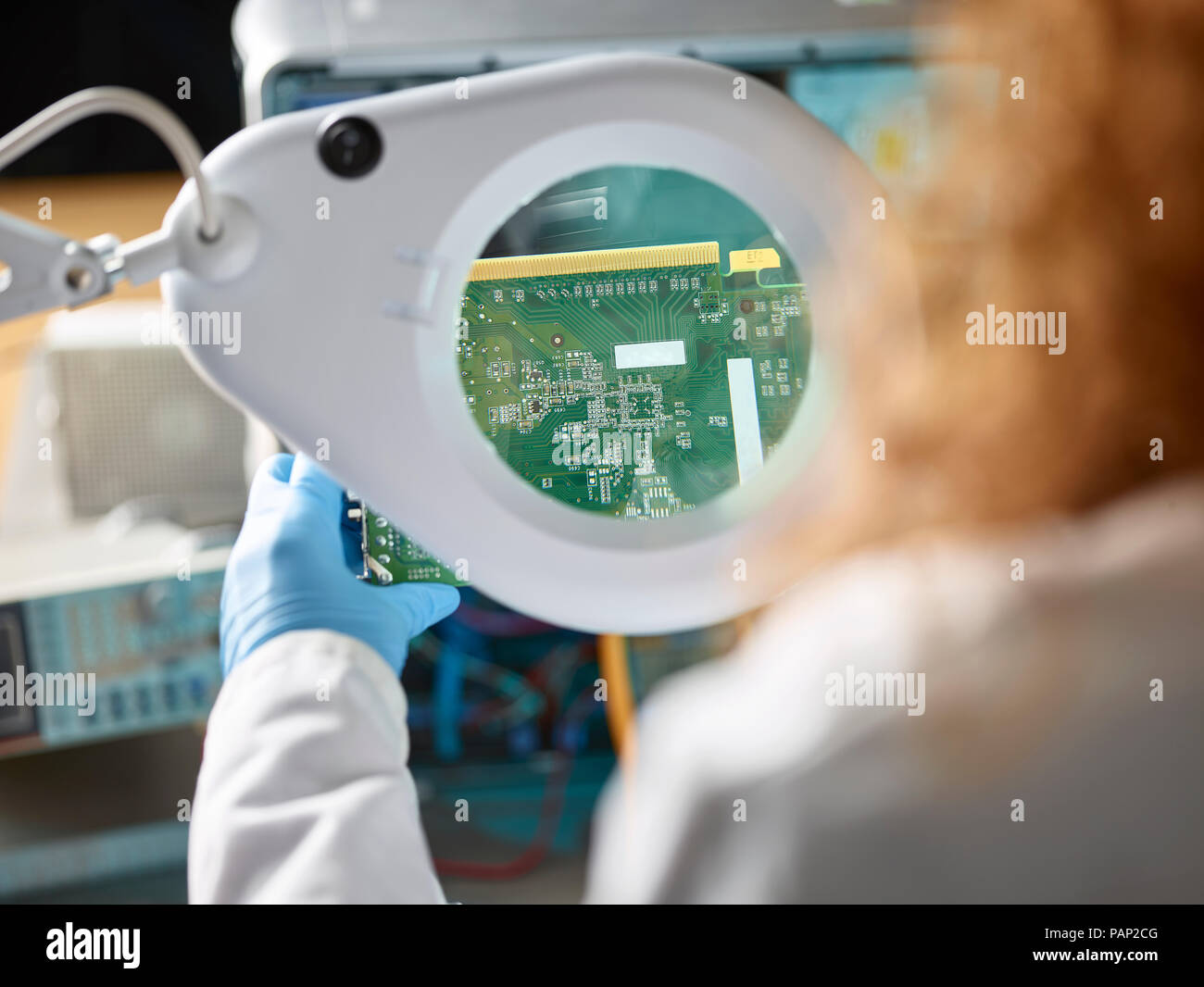 Female technician checking circuit board with magnifier Stock Photo