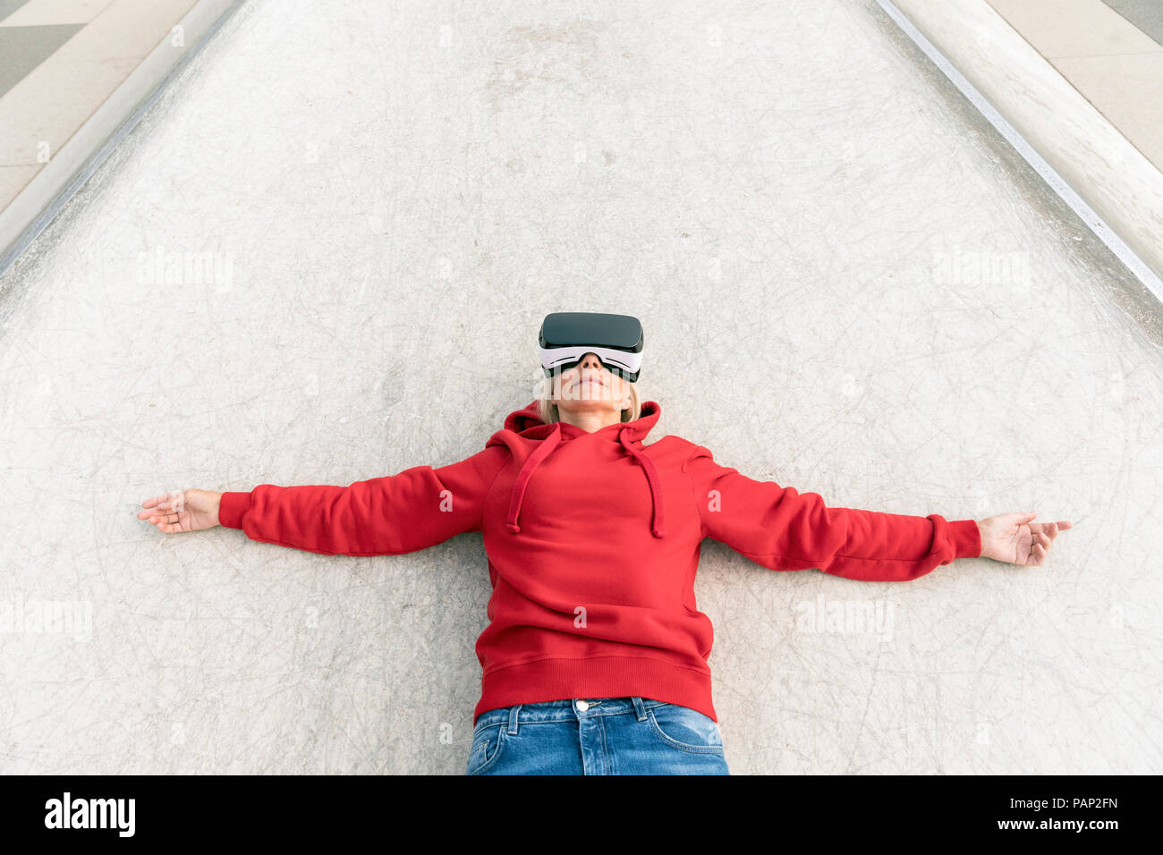Senior woman lying on the ground wearing VR glasses Stock Photo