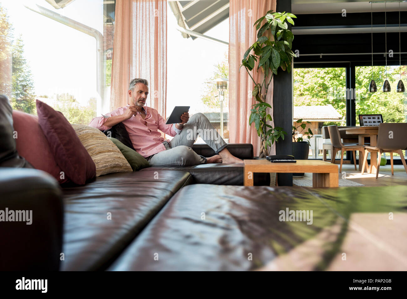 Mature man sitting on couch at home using a tablet Stock Photo