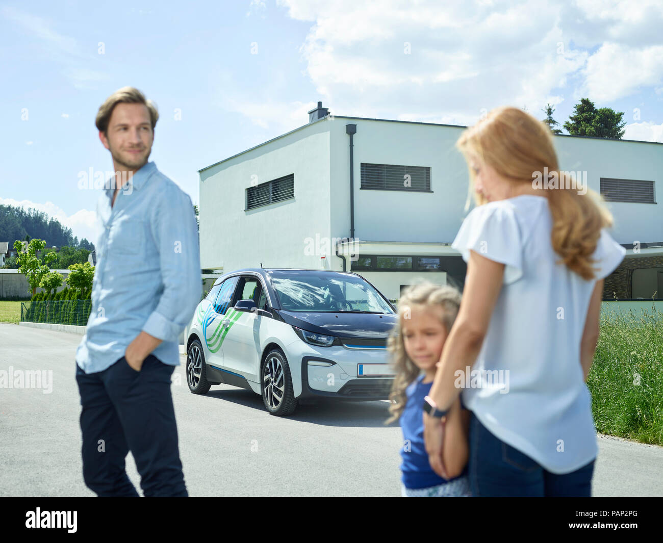 Family with electric car in front of house Stock Photo