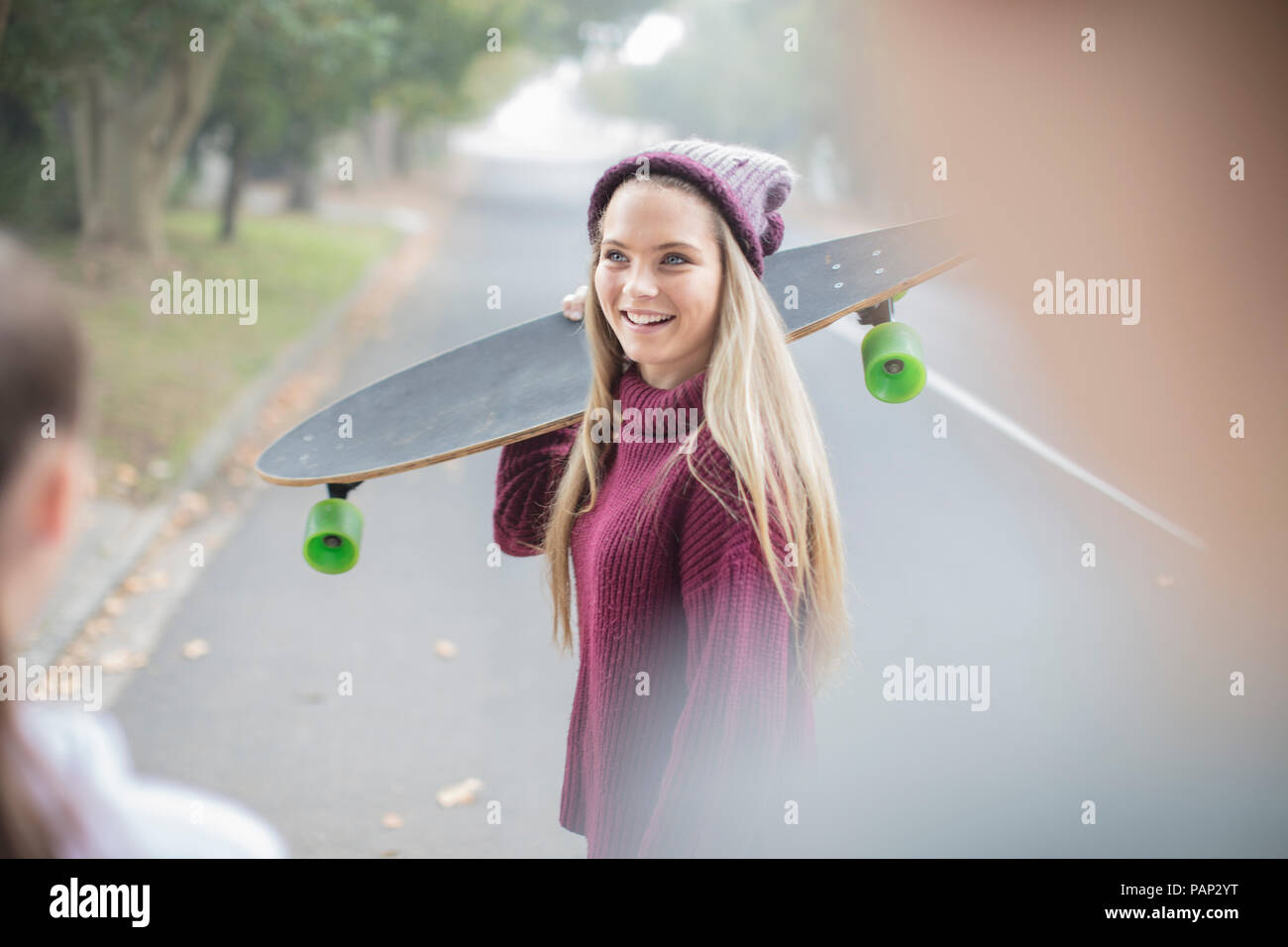 Smiling teenage girl holding skateboard meeting with friend Stock Photo