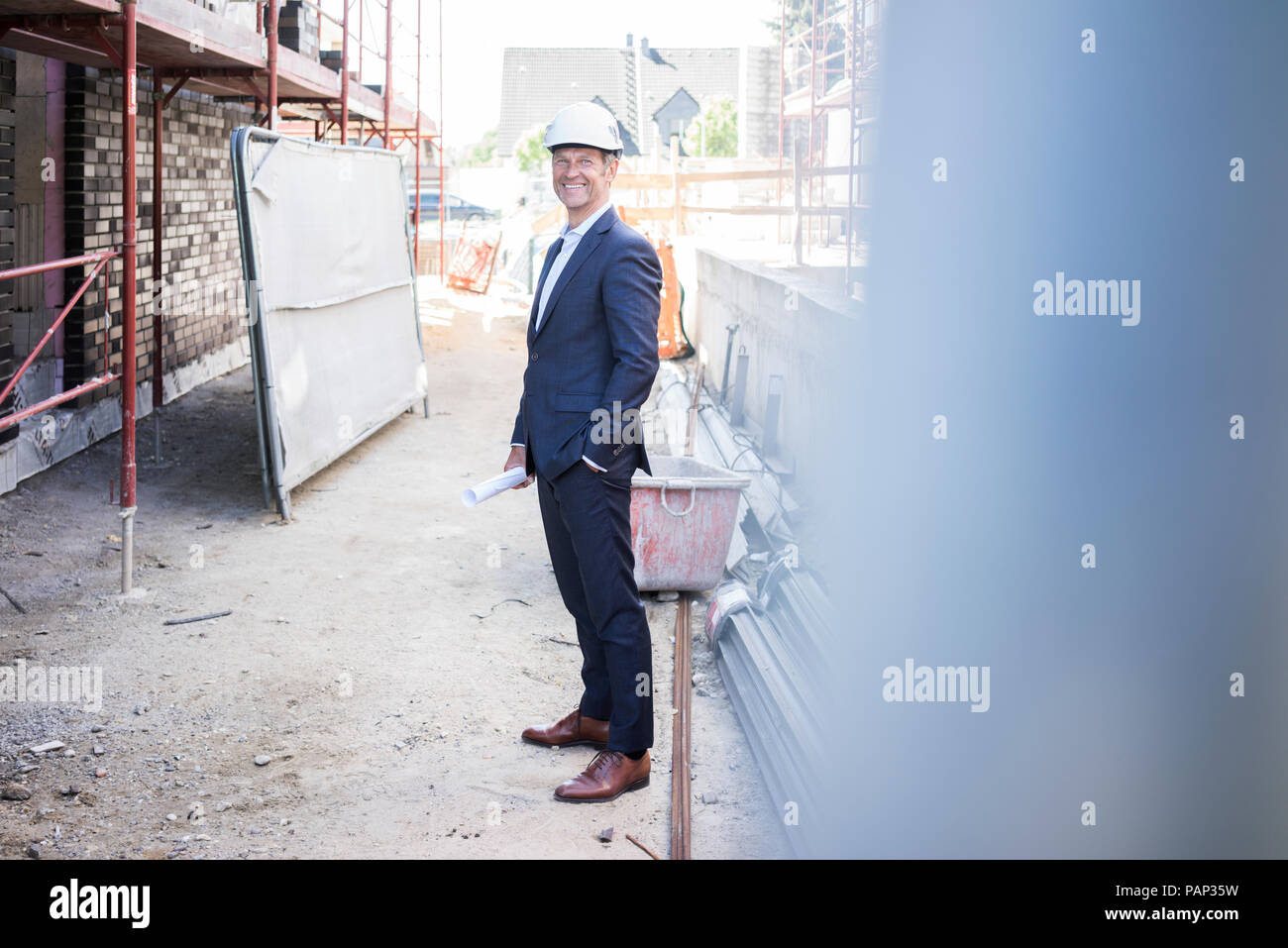 Smiling architect wearing hard hat standing on construction site Stock Photo