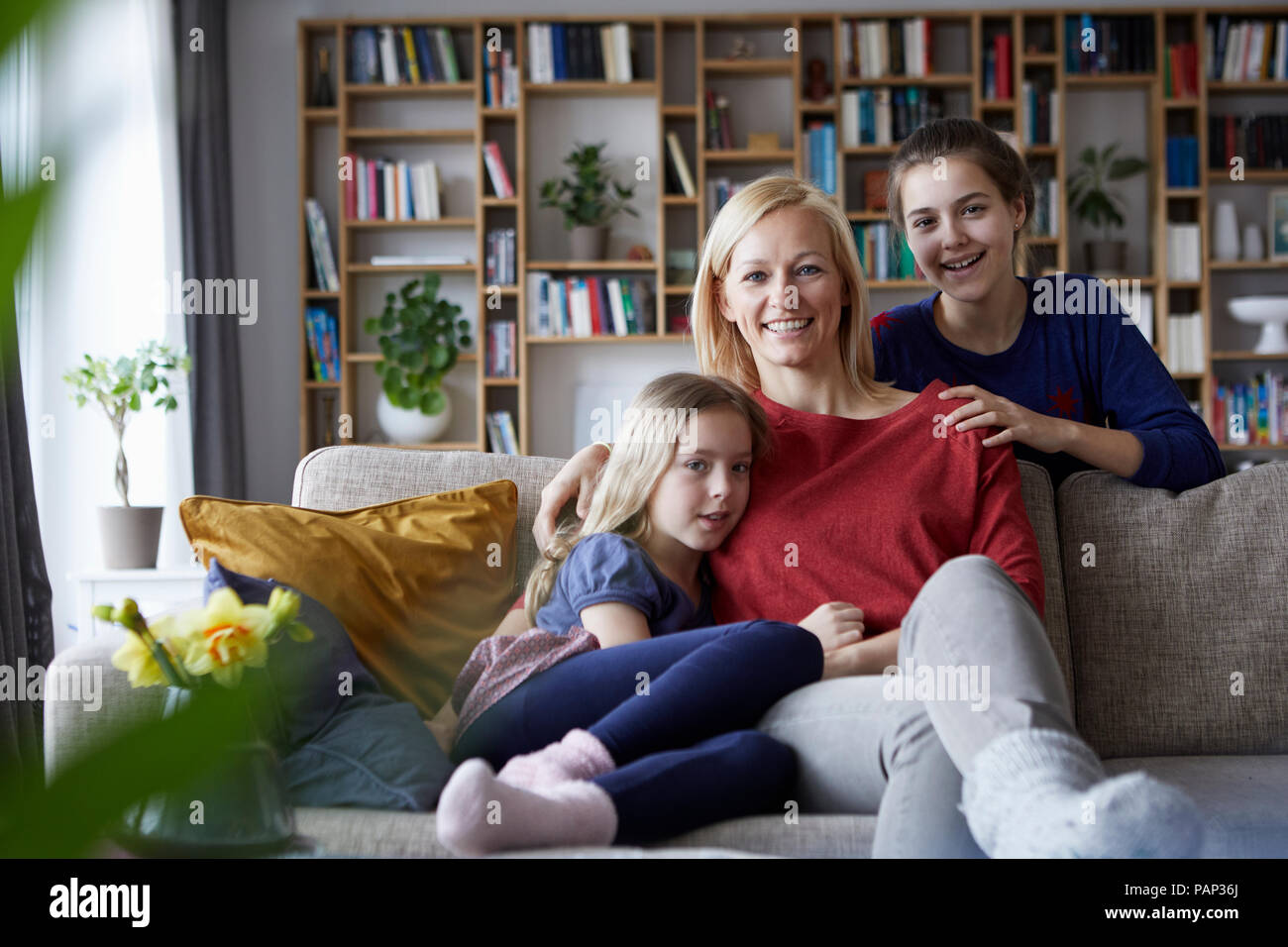 Mother and her daughters cuddling and having fun, sitting on couch Stock Photo
