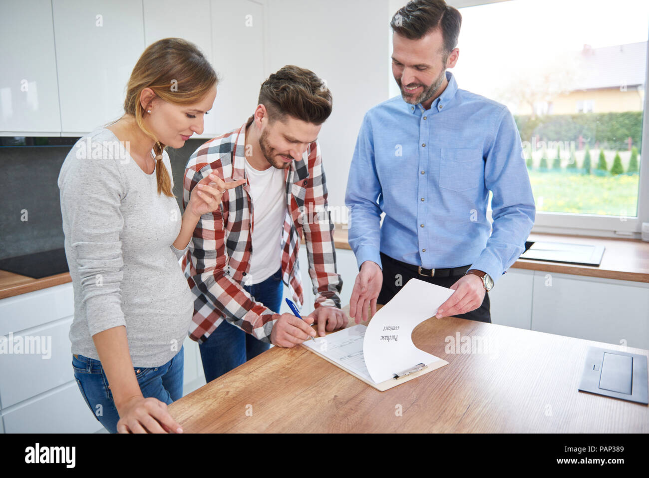 Couple with real estate agent signing contract in kitchen of new apartment Stock Photo