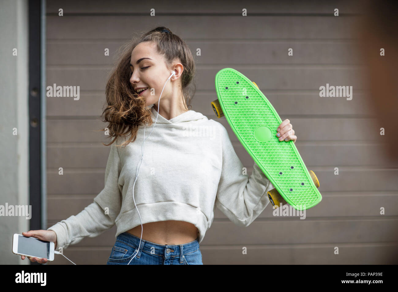 Carefree teenage girl dancing while holding skateboard and listening to music Stock Photo