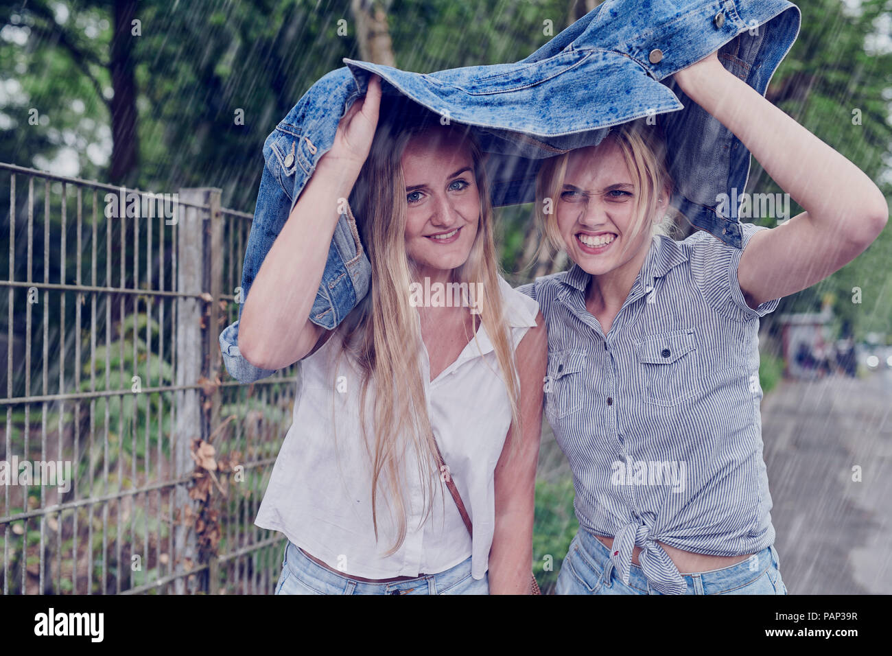 Two young women shletering from rain with a denim jacket Stock Photo