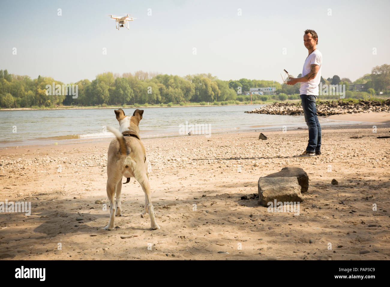 Man with a dog flying drone at a river Stock Photo