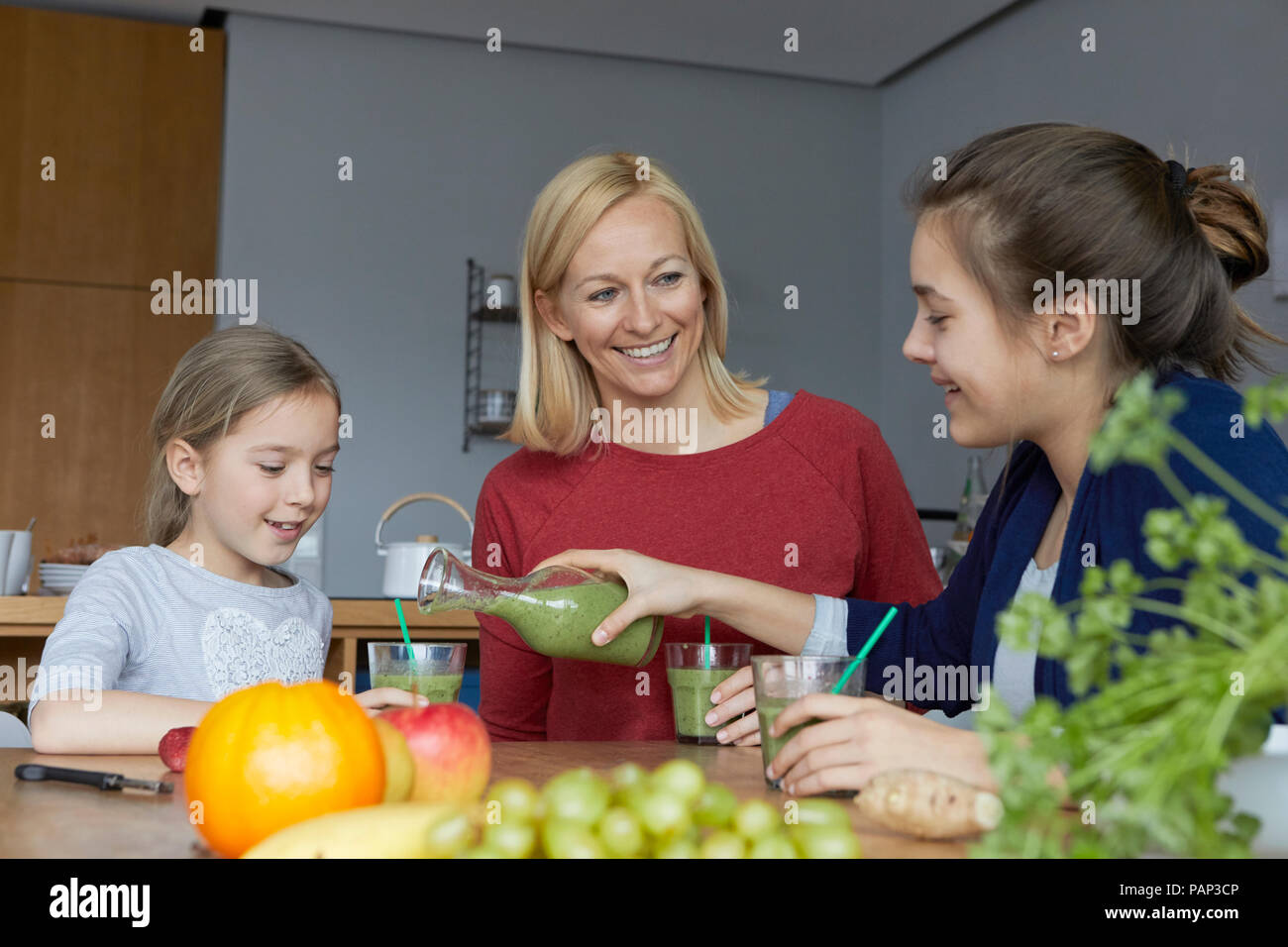 Mother with daughters sitting in kitchen, drinking homemade fruit smoothie Stock Photo