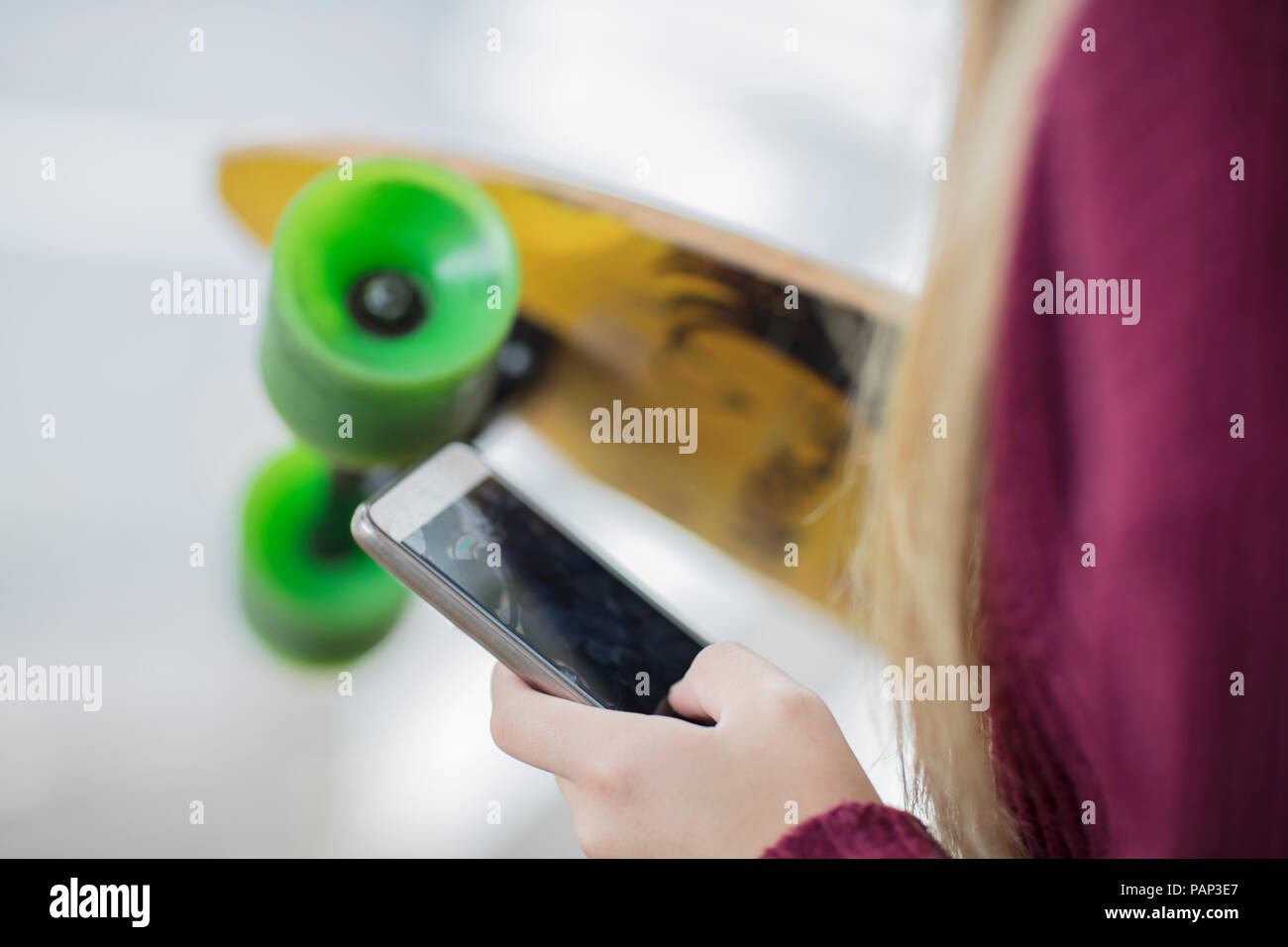 Close-up of teenage girl holding skateboard and cell phone Stock Photo