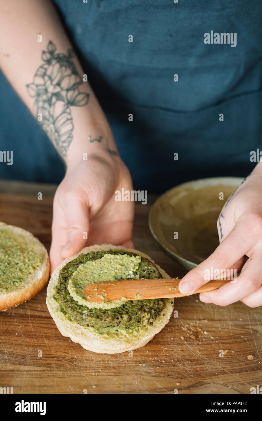 Woman preparing vegan burger, spreading avocado cream on fritter Stock Photo