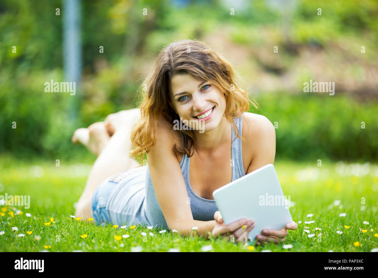 Smiling young woman lying on meadow, using tablet Stock Photo
