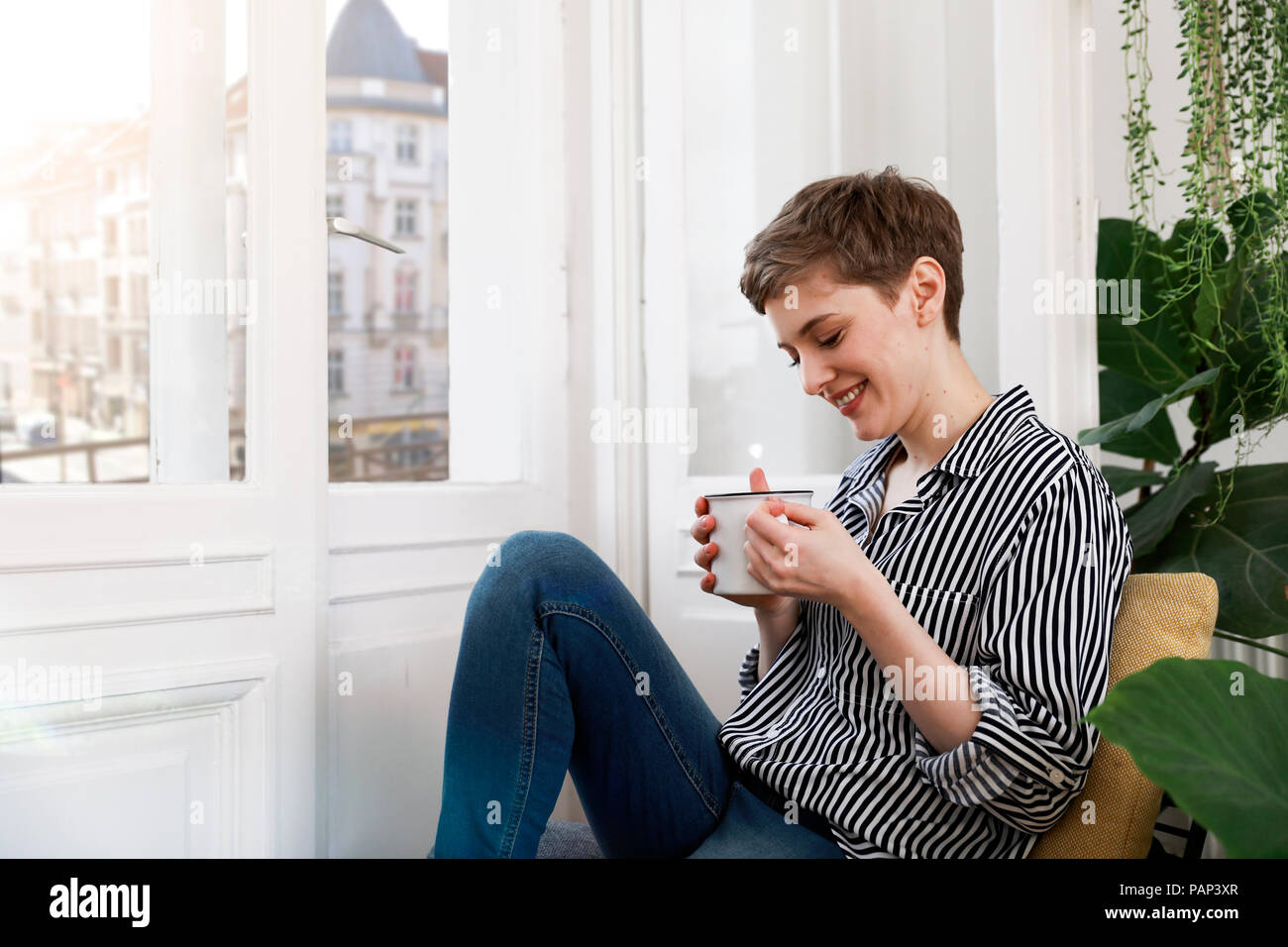 Happy woman sitting relaxed at window, drinking coffee Stock Photo
