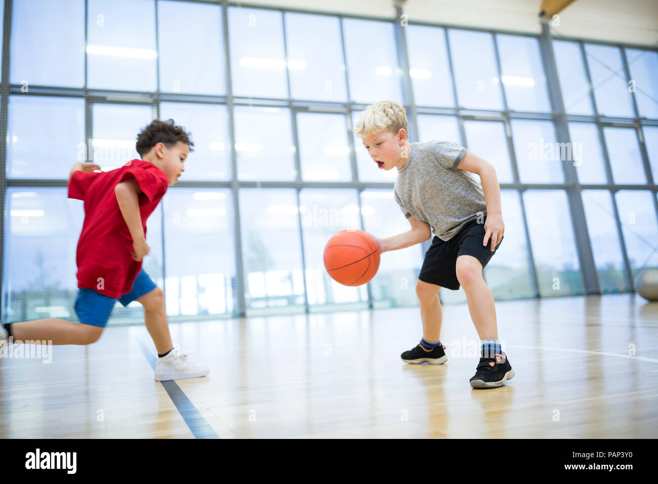 Two schoolboys playing basketball in gym class Stock Photo