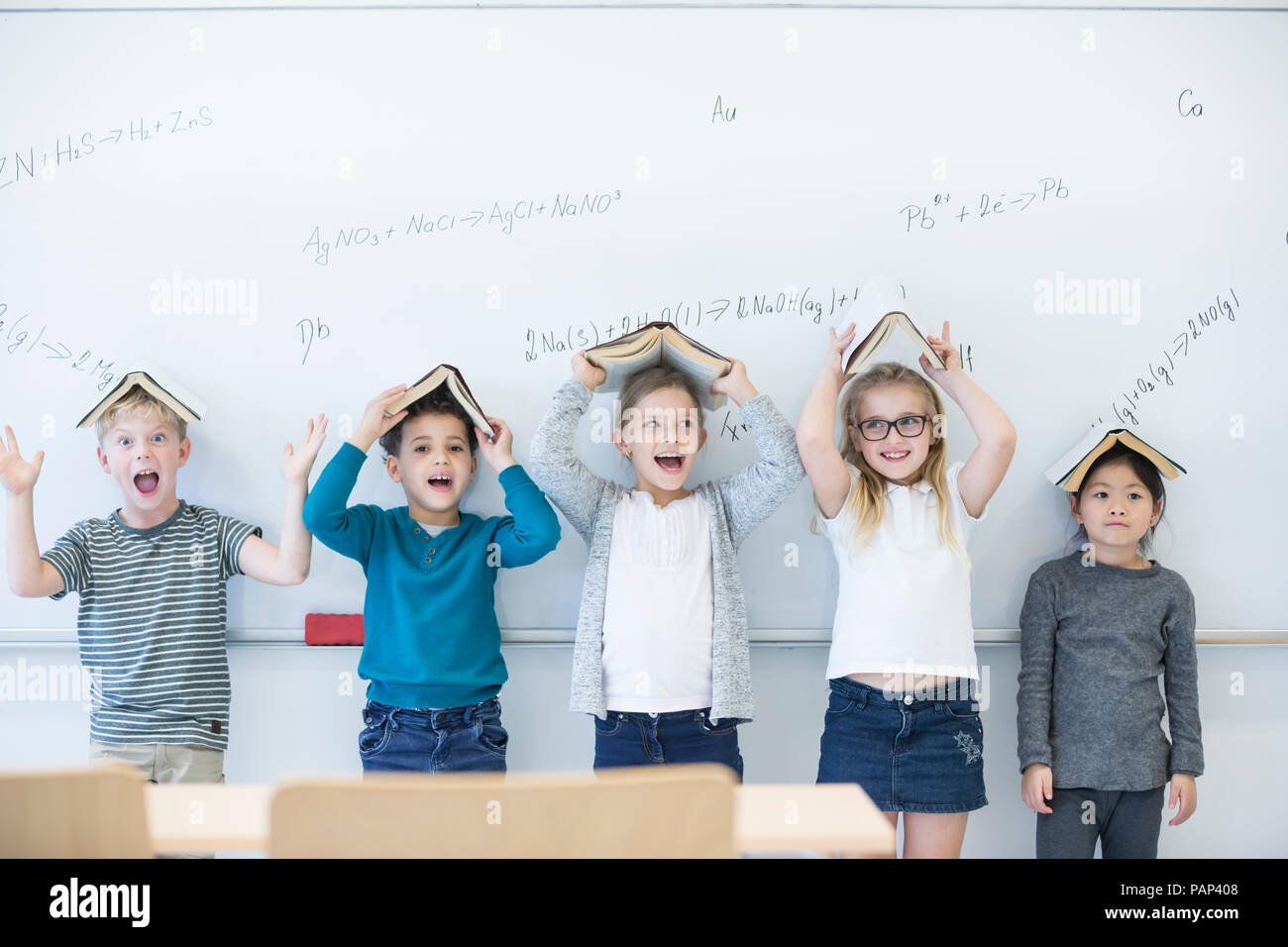 Happy pupils with books above their heads standing at whiteboard with formulas in class Stock Photo