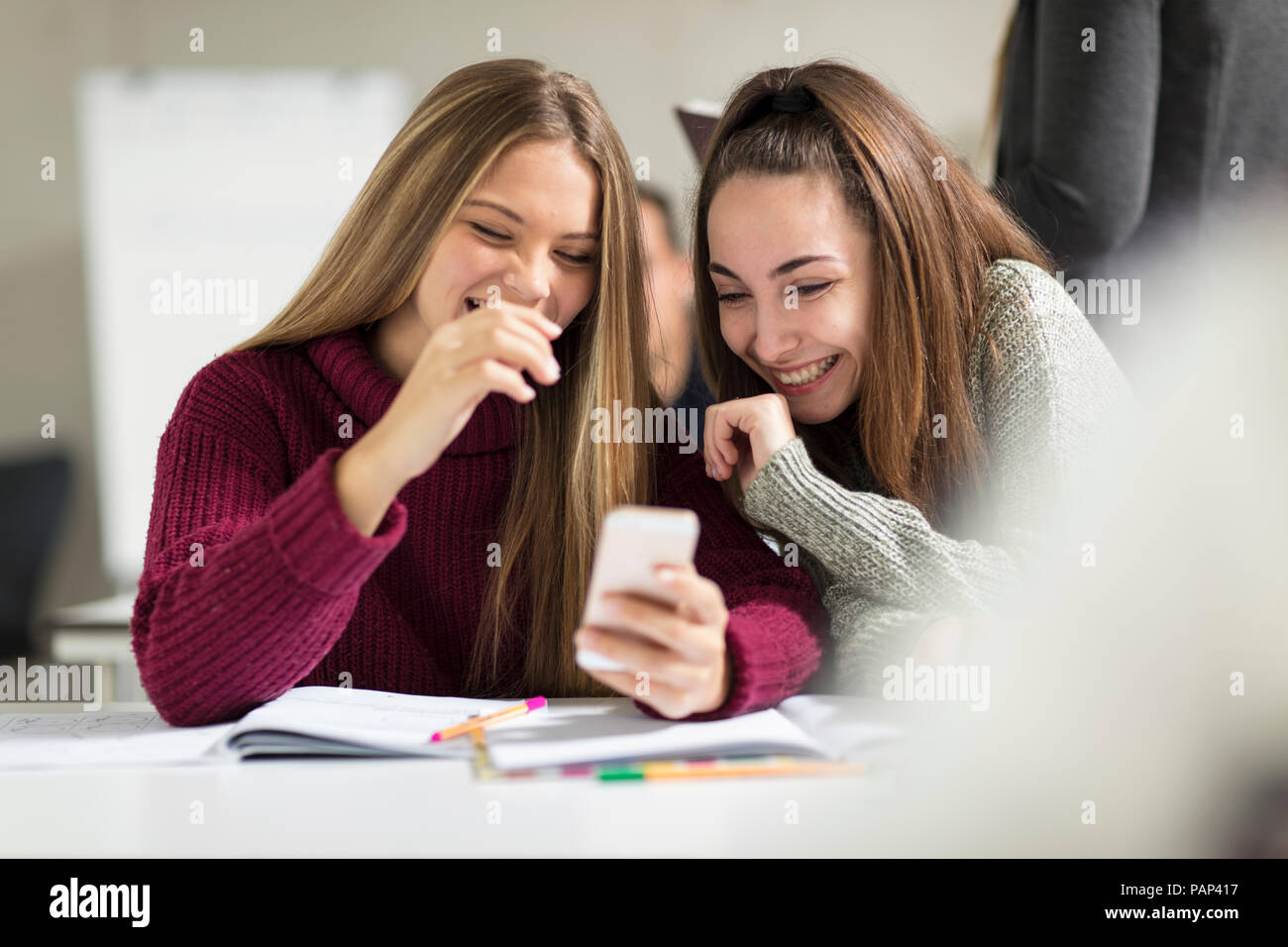 Happy teenage girls in class looking at cell phone Stock Photo