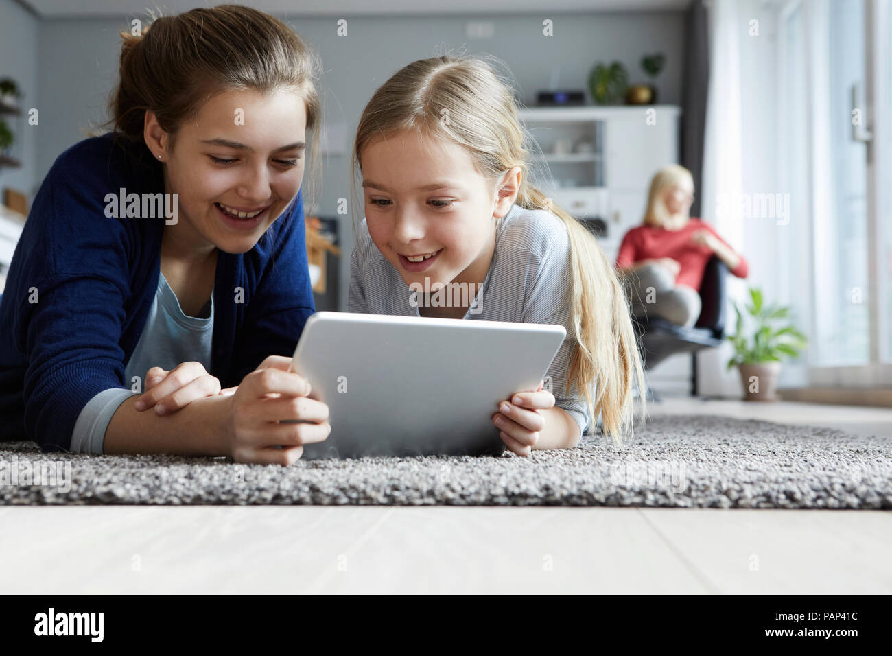 Teo sisters lying on floor, playing with digital tablet Stock Photo