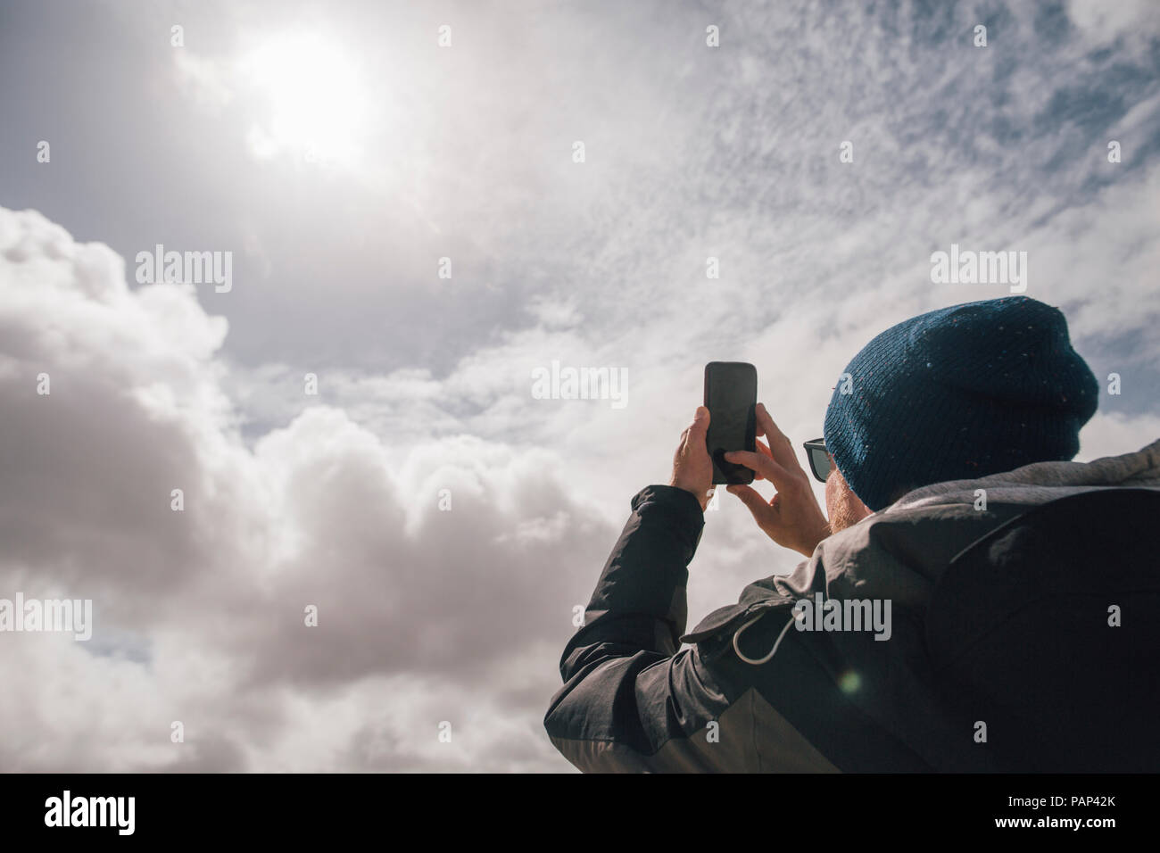Man holding up cell phone under sunny sky with clouds Stock Photo