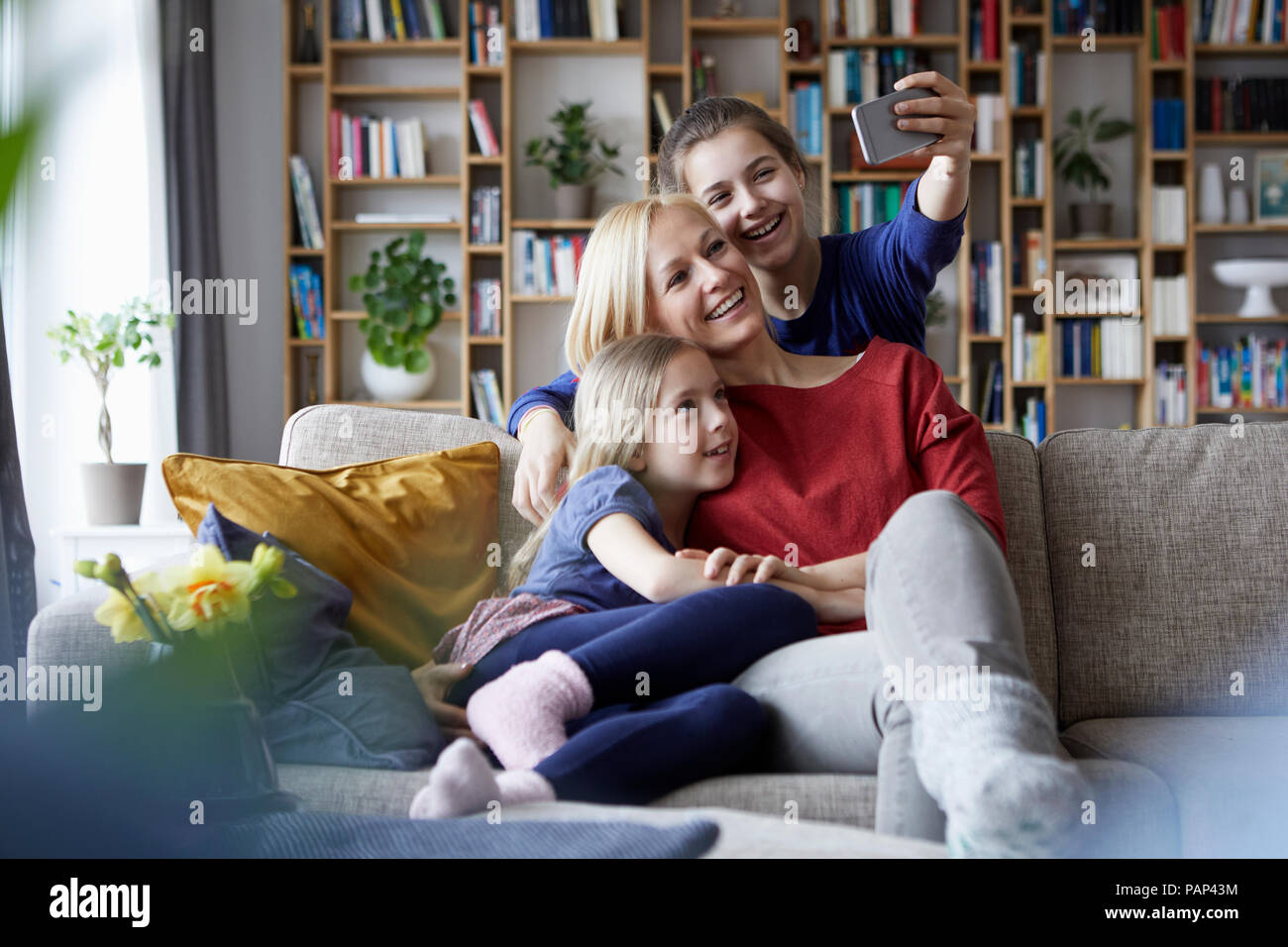 Mother and her daughters sitting on couch,taking smartphone selfies Stock Photo