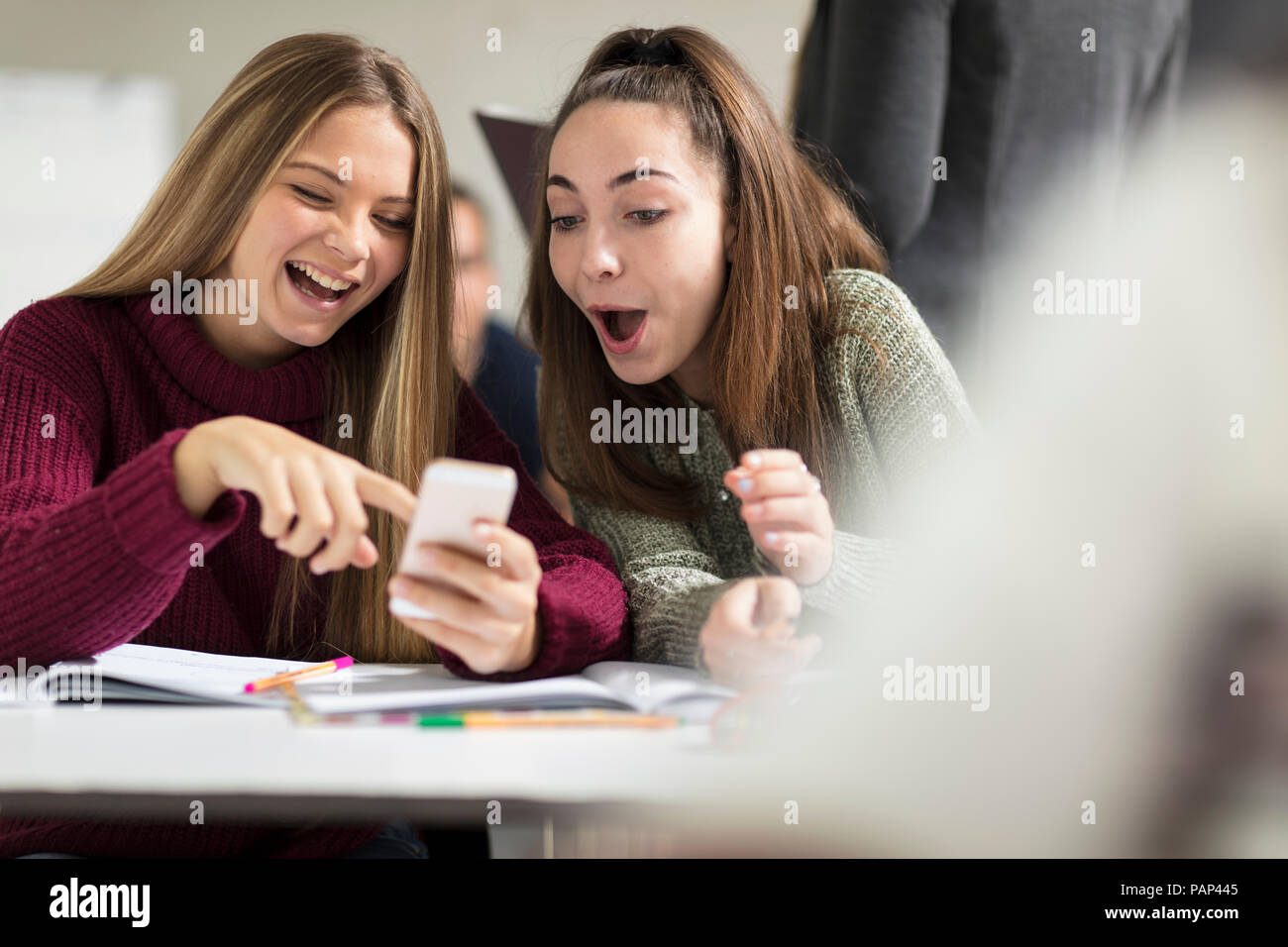 Happy teenage girls in class looking at cell phone Stock Photo