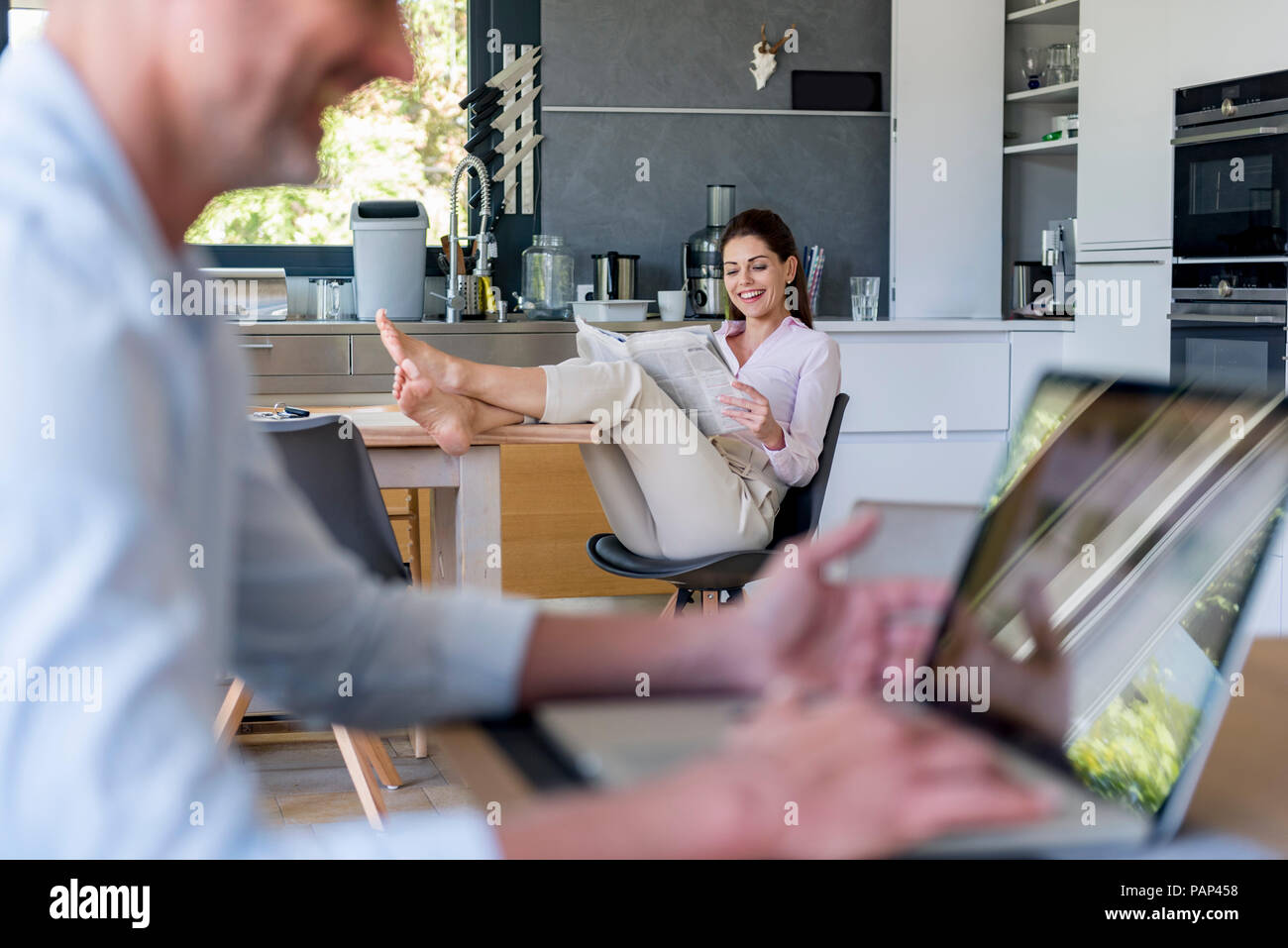 Couple at home with man using a laptop and woman reading newspaper Stock Photo