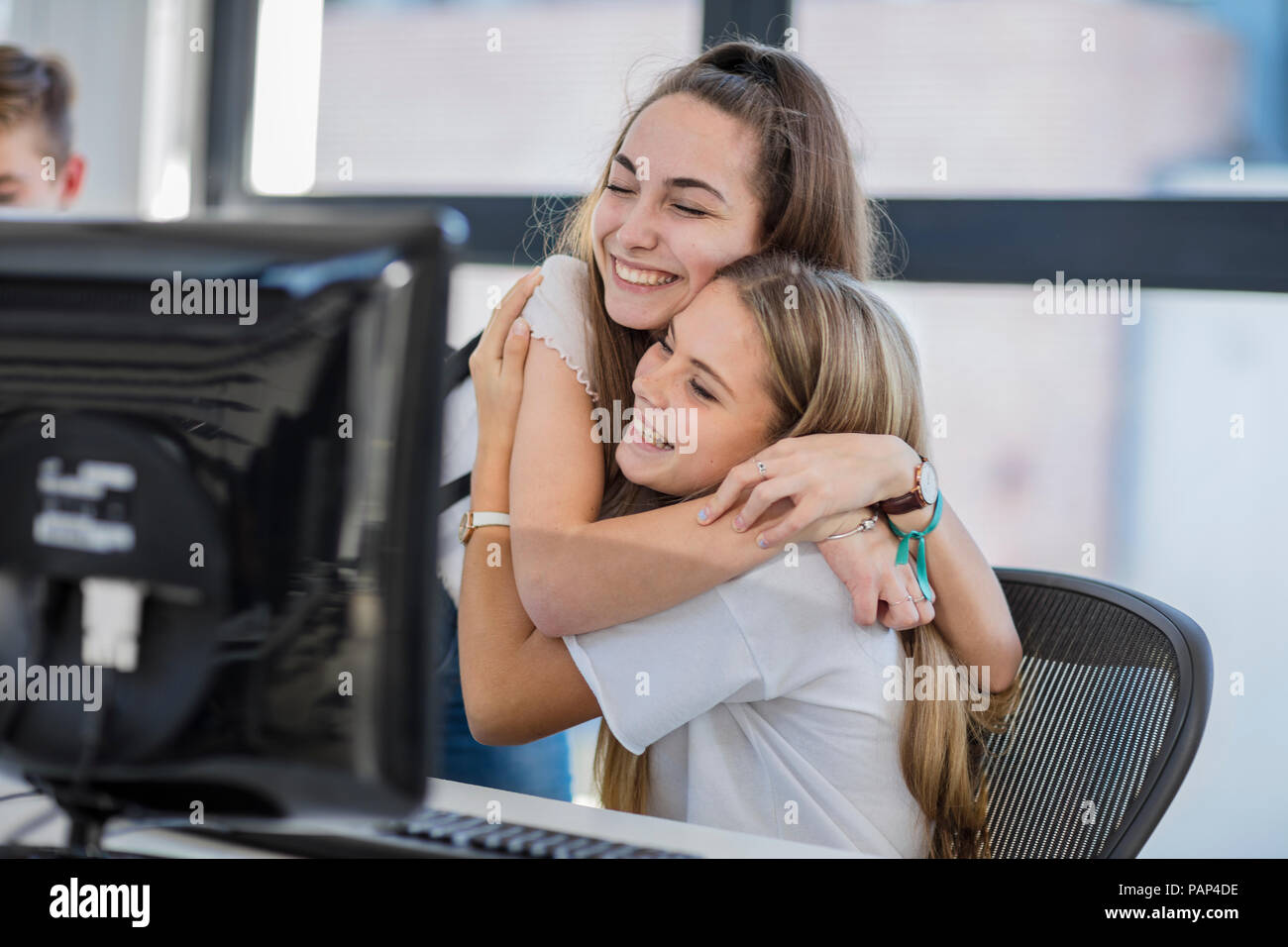 Happy teenage girls hugging in computer class Stock Photo