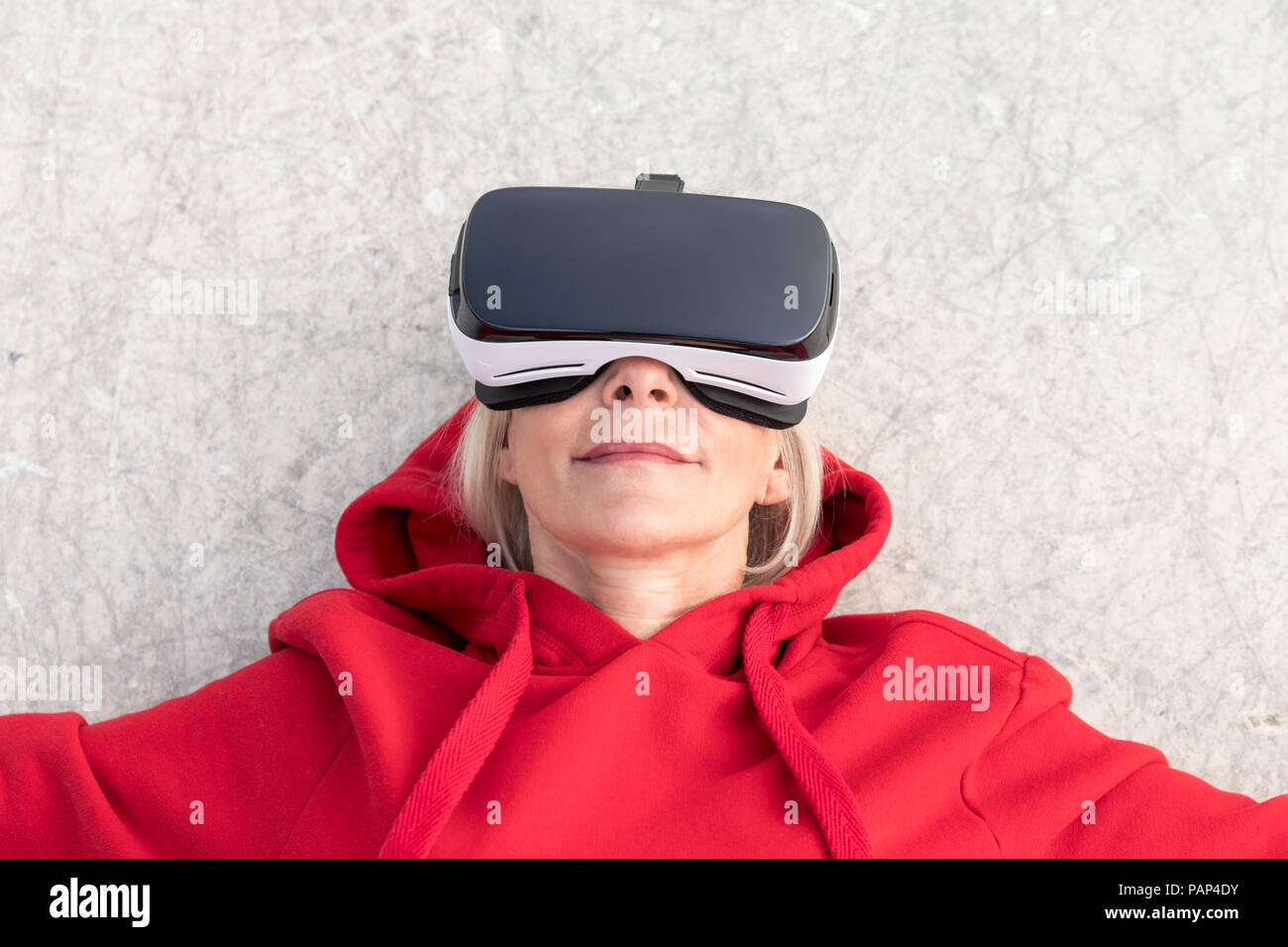 Senior woman lying on the ground wearing VR glasses Stock Photo