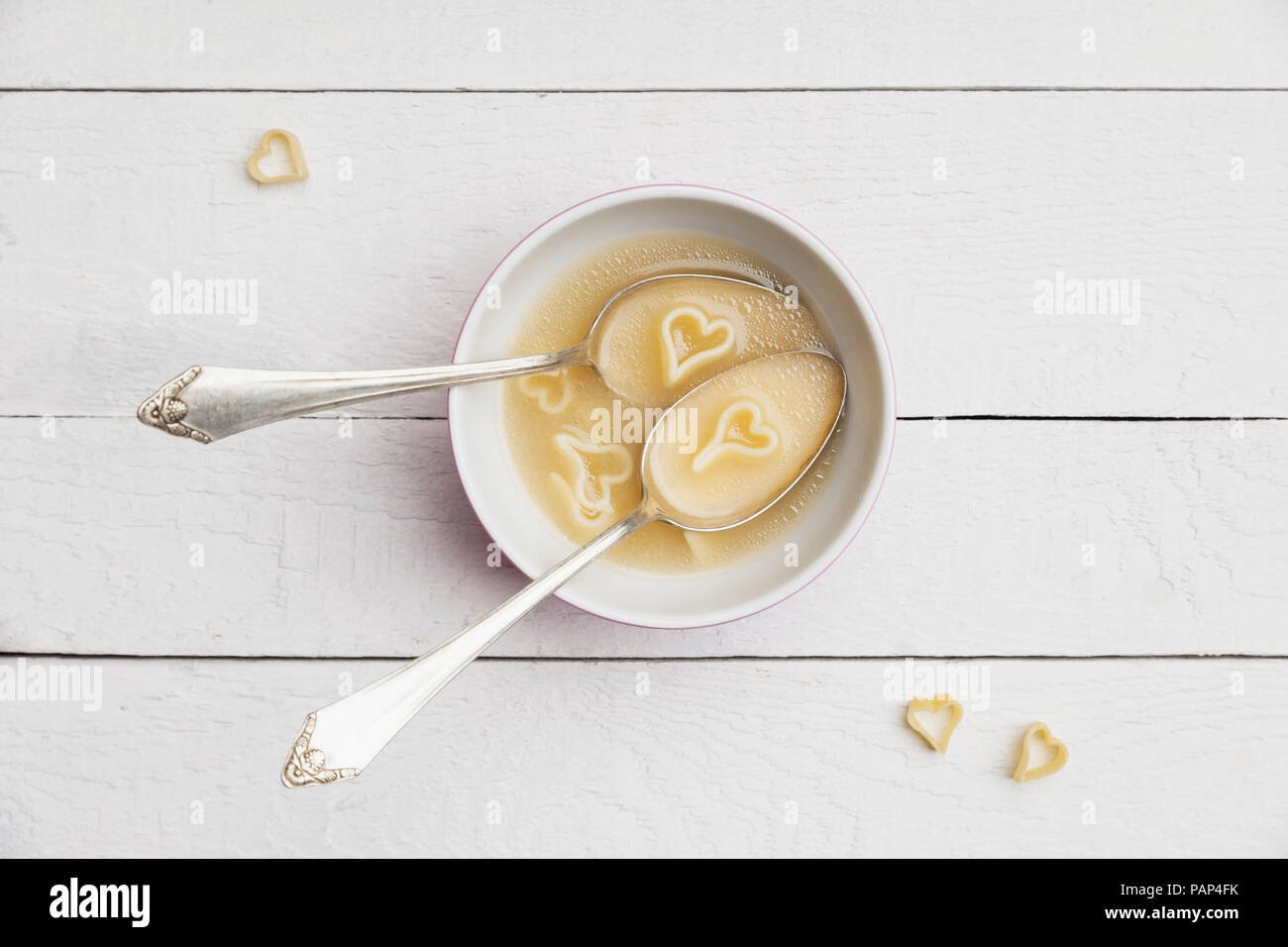 Two silver spoons in bowl of chicken soup with heart-shaped noodles Stock Photo