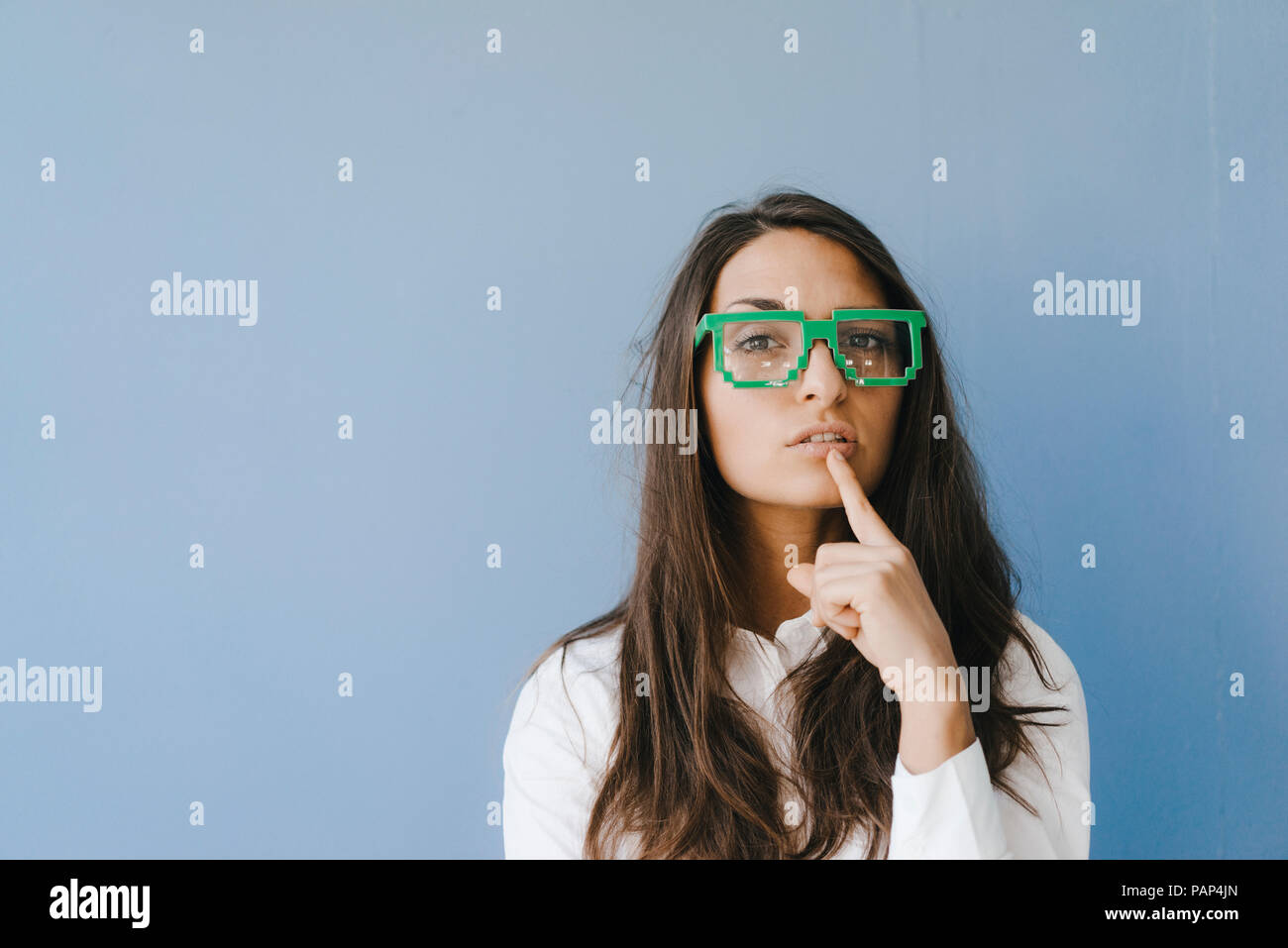 Young woman wearing pixel glasses, putting finger on mouth Stock Photo