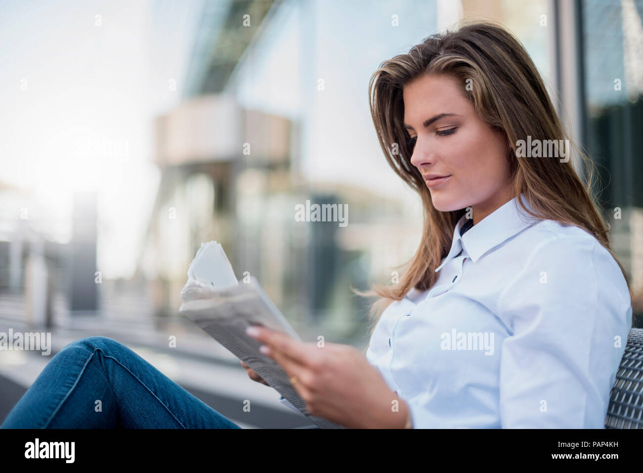 Portrait of young businesswoman sitting on bench reading newspaper Stock Photo