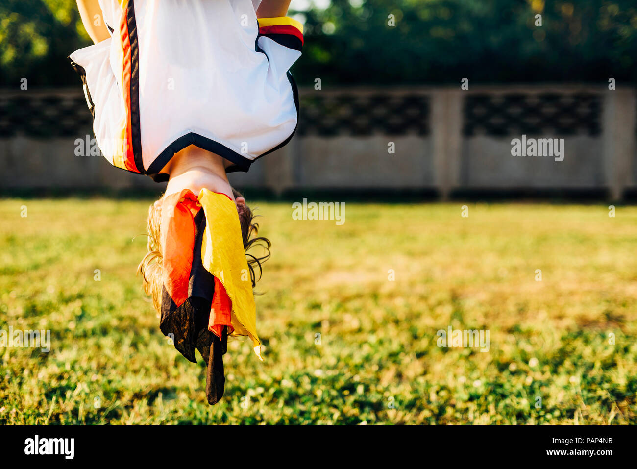 Boy in German football shirt, hanging upside down with face covered by German flag Stock Photo