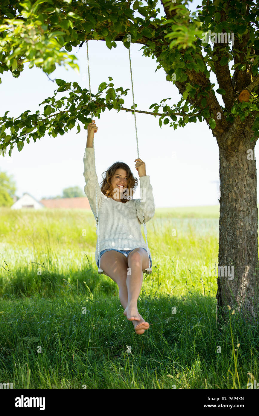 Smiling young woman sitting on swing Stock Photo - Alamy