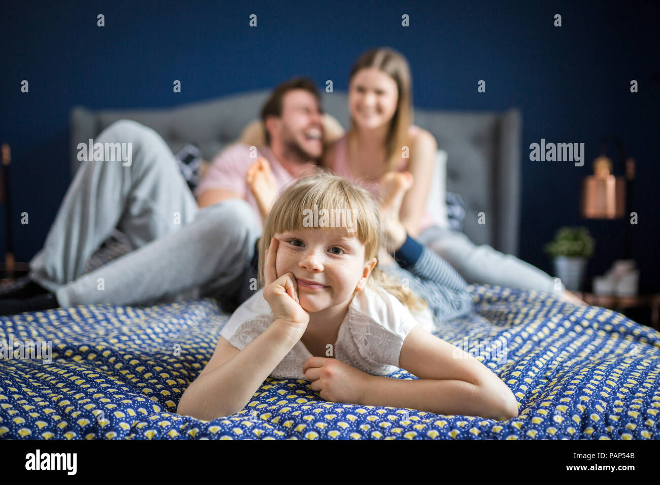 Cheeky little girl lying on bed with her parents Stock Photo