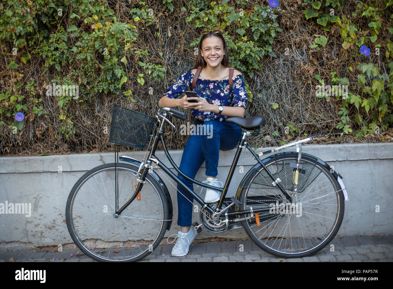 Portrait of smiling teenage girl with cell phone and bicycle Stock Photo
