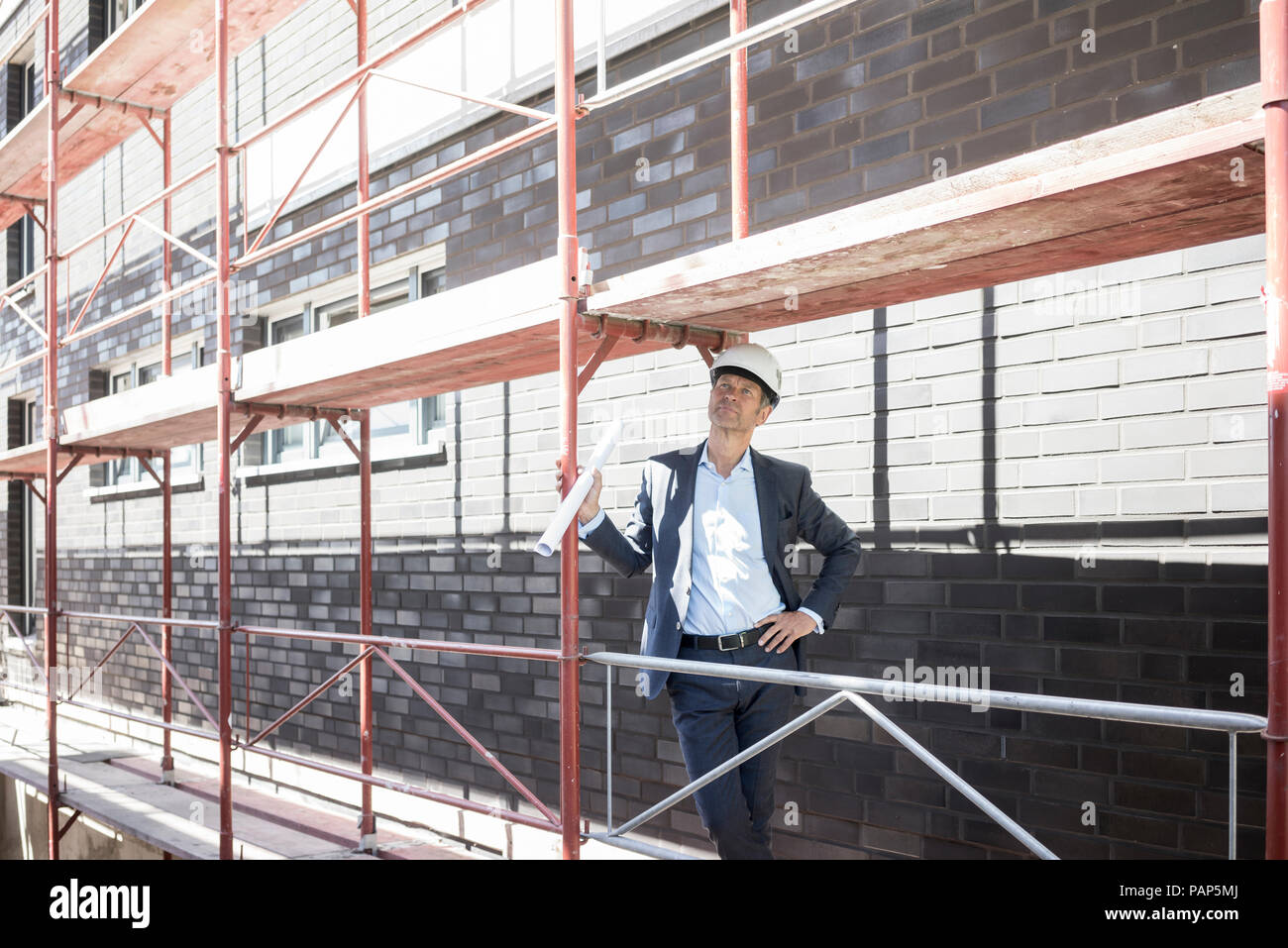 Architect wearing hard hat standing on scaffolding on construction site Stock Photo