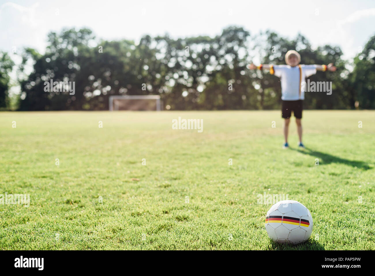 Boy with outstretched arms standing on soccer field between German soccer ball and goal Stock Photo