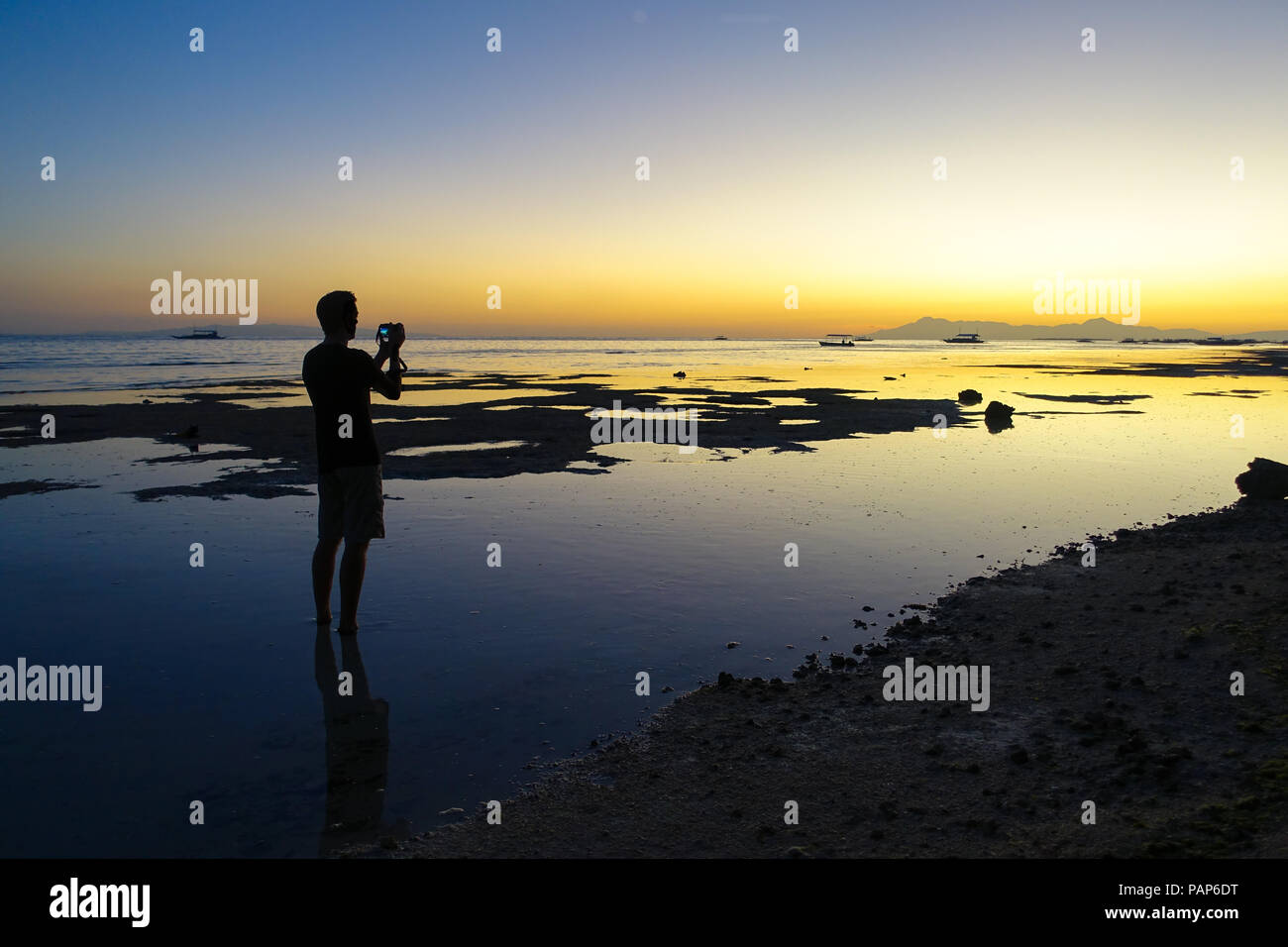 Silhouette of photographer tourist taking photos of a serene sunset beach at low tide - Panglao, Philippines Stock Photo