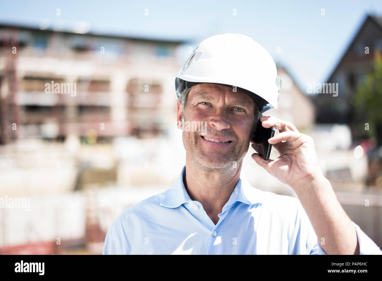 Portrait of smiling man wearing hard hat on cell phone on construction site Stock Photo