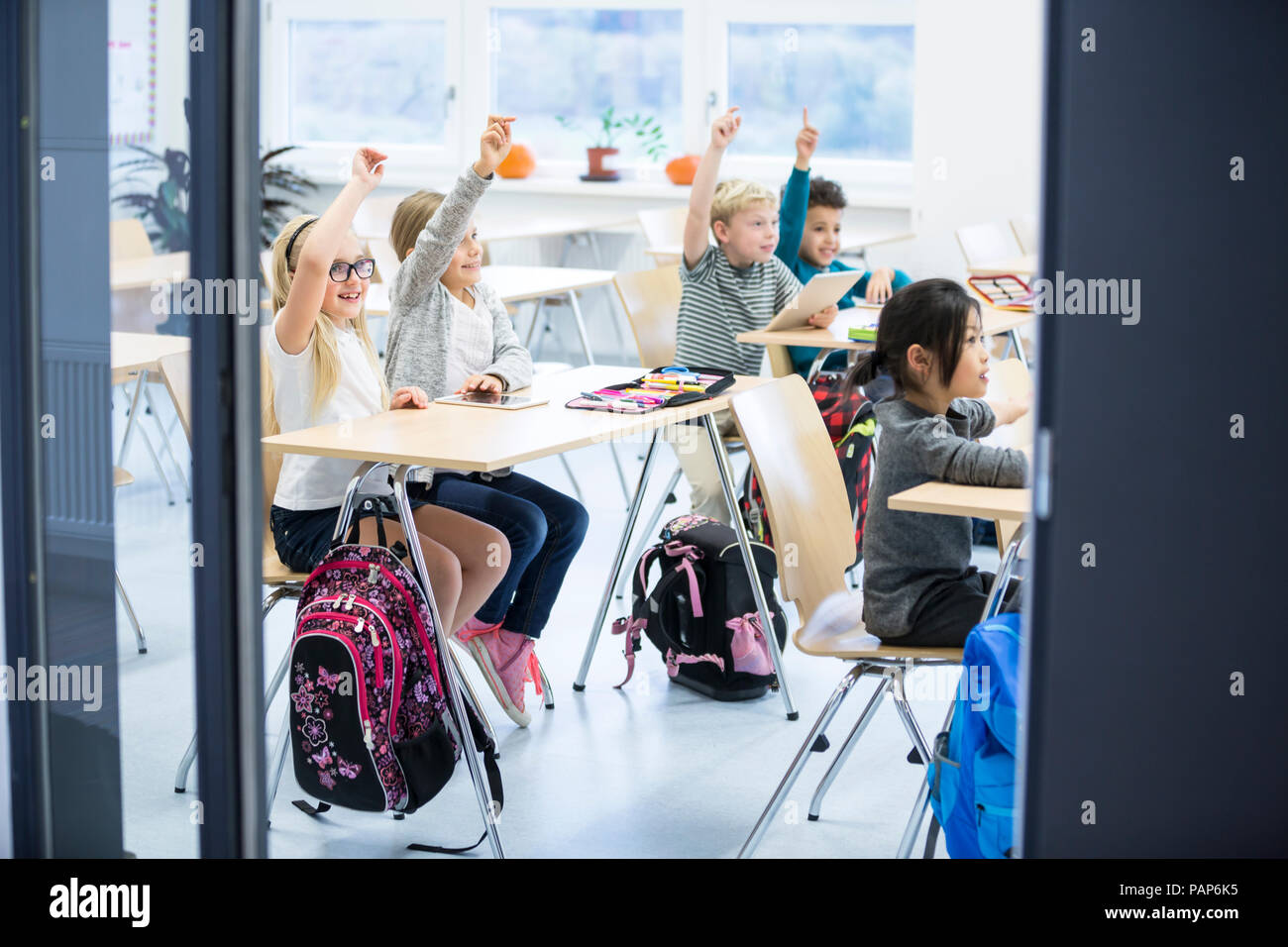 Happy pupils raising their hands in class Stock Photo