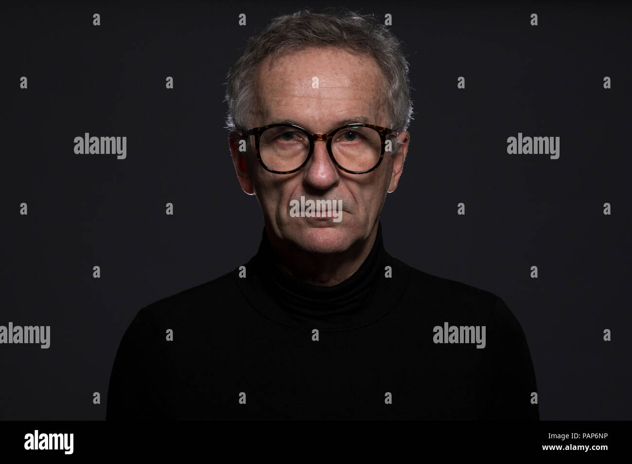 Portrait of serious senior man wearing glasses in front of dark background Stock Photo