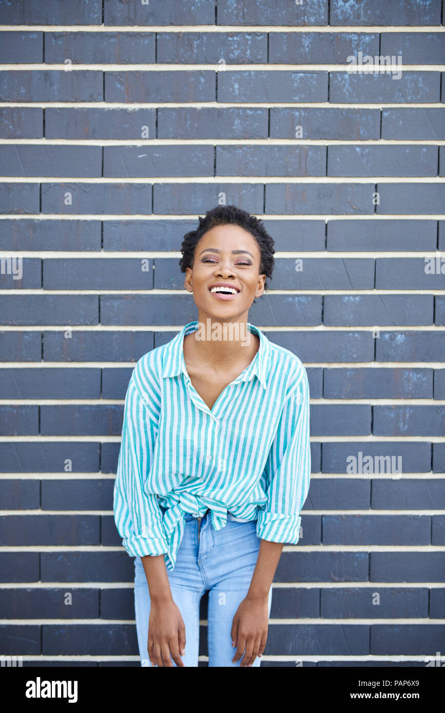 Portrait of laughing woman standing in front of grey facade Stock Photo
