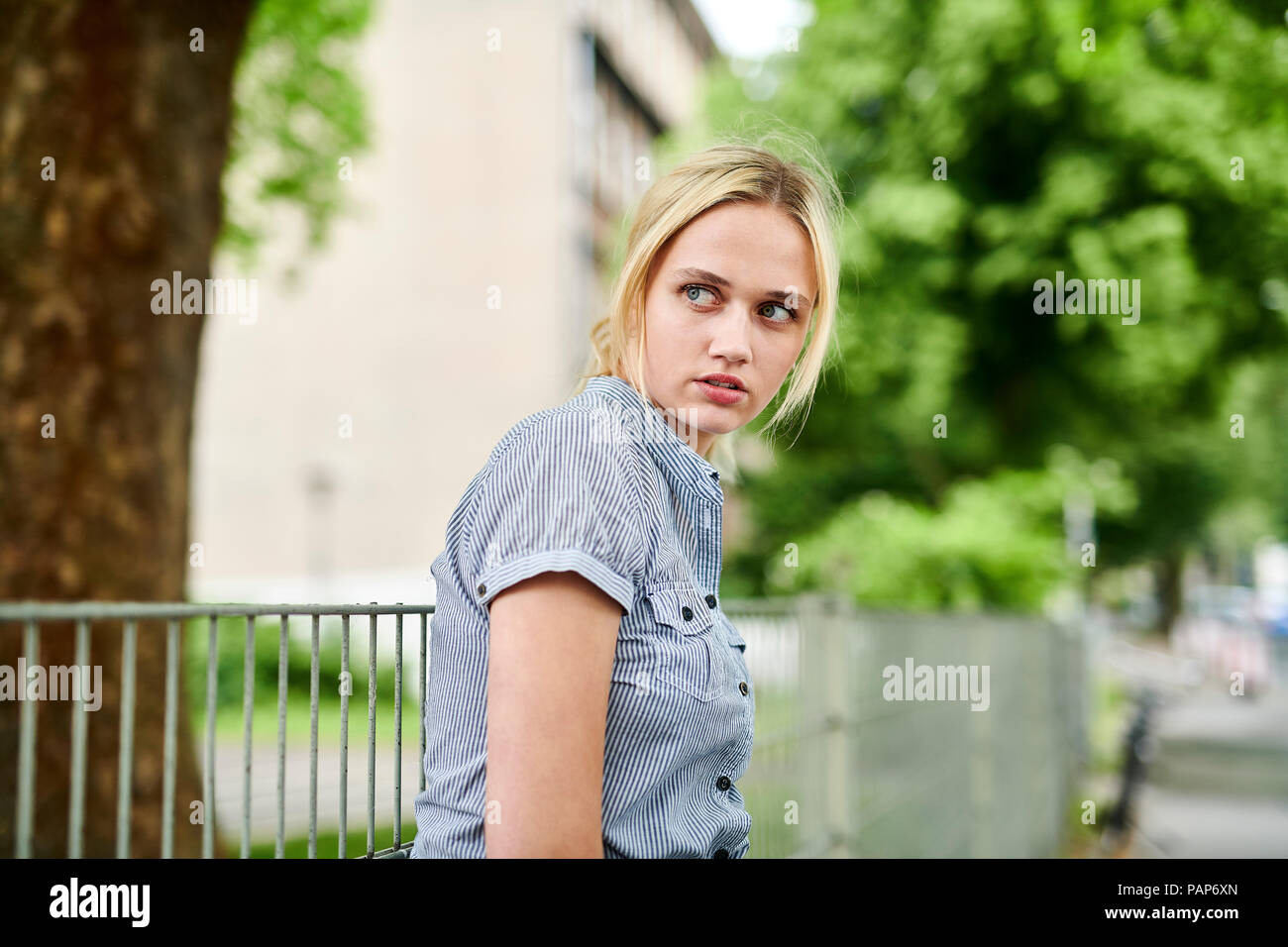 Serious blond young woman at a fence Stock Photo